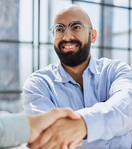 Smiling bearded man in glasses shaking hands in bright modern office setting.