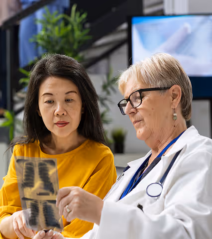 Female doctor showing lung X-rays to female patient in medical office.